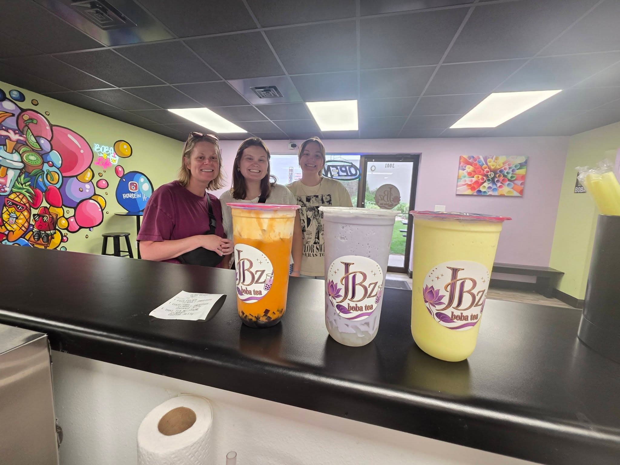 Three JBz drinks on the counter: an iced fruit tea with mango, a coconut cream, and a bright yellow tea